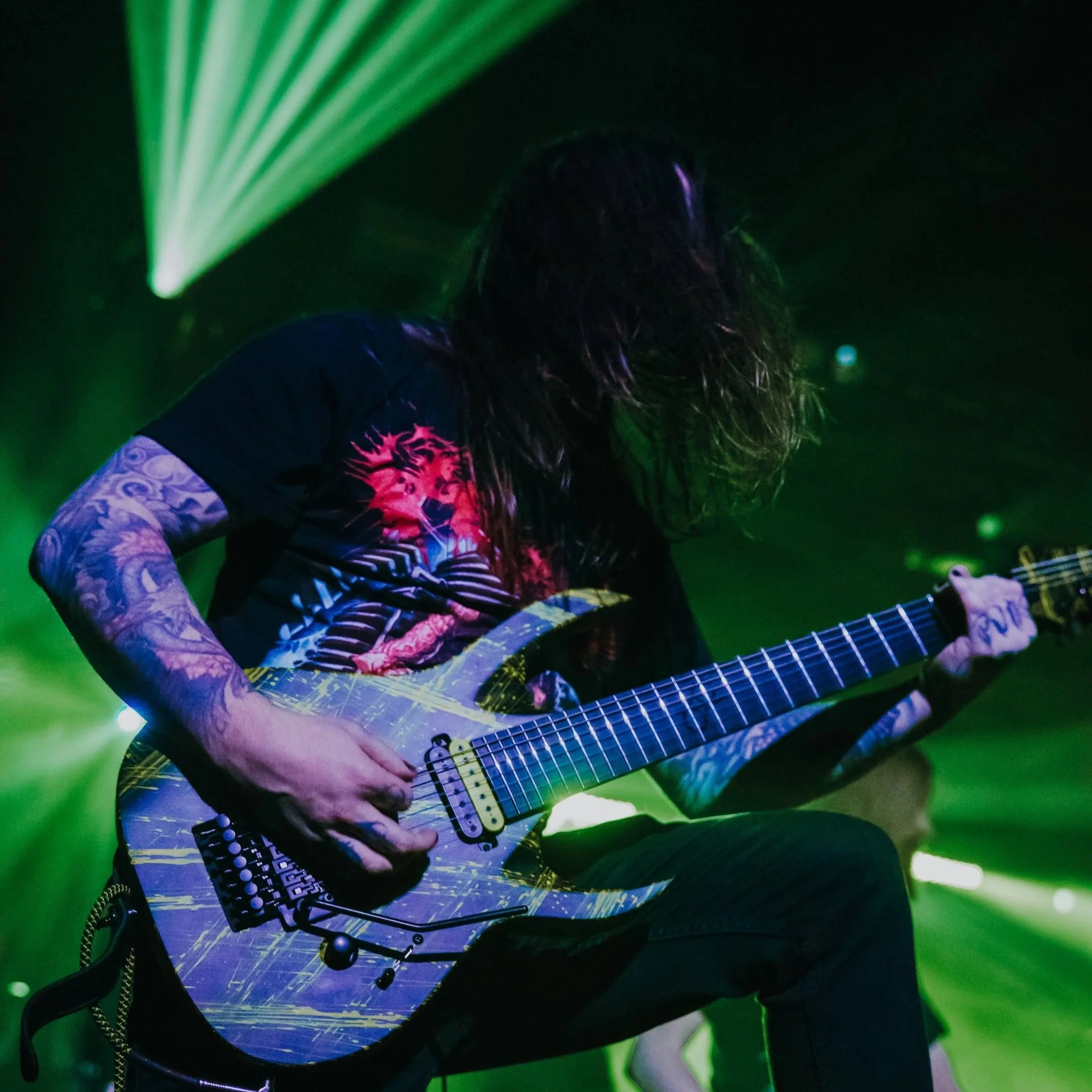 A person with long hair playing an electric guitar on stage with green lighting.