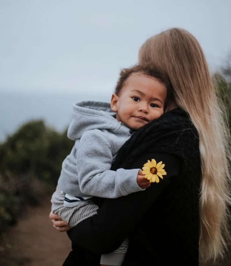 Woman in black holding sad child with flower in hand outdoors