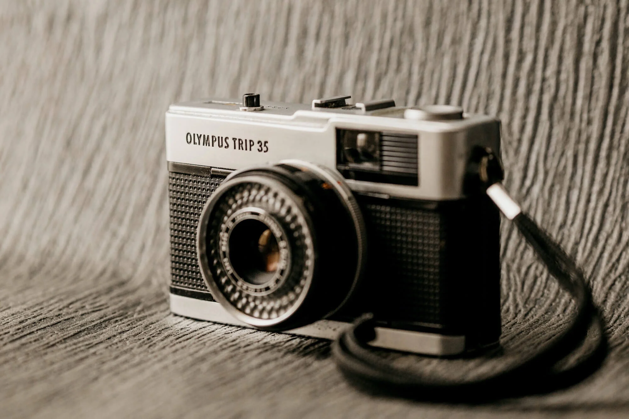 A vintage Olympus Trip 35 camera sitting on a textured gray surface with a gray fabric background.