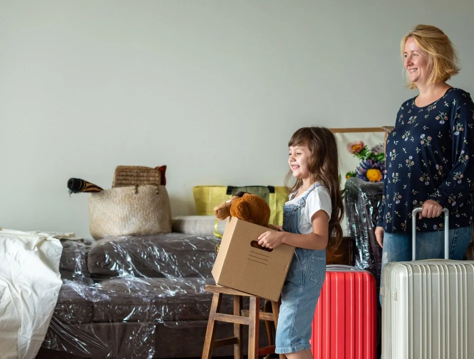 Grandmother with suitcases and granddaughter with box with teddybear moving out