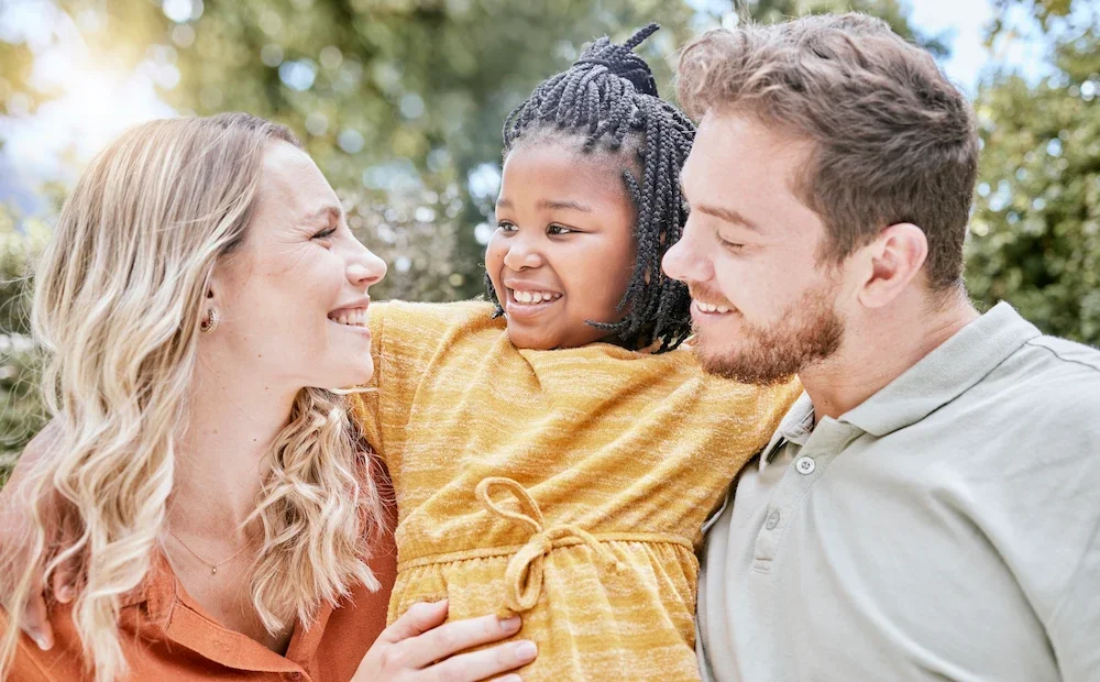 A smiling family of three outdoors, with a woman, man, and young girl, sharing a joyful moment.