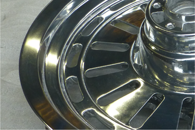 A close-up of a shiny metal truck wheel rim with a central hub, placed on a concrete floor.