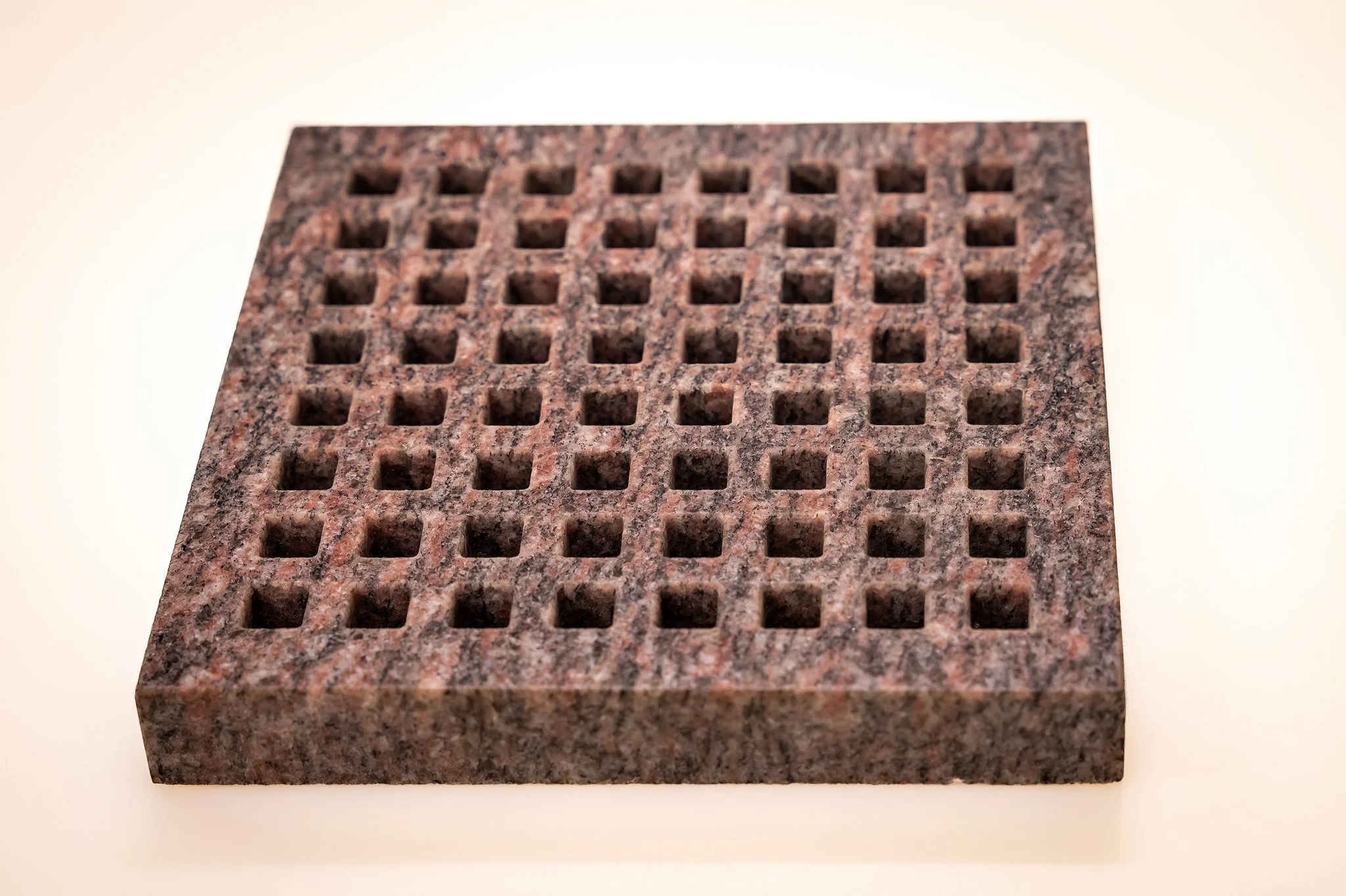 A rectangular granite comb with evenly spaced square teeth.
