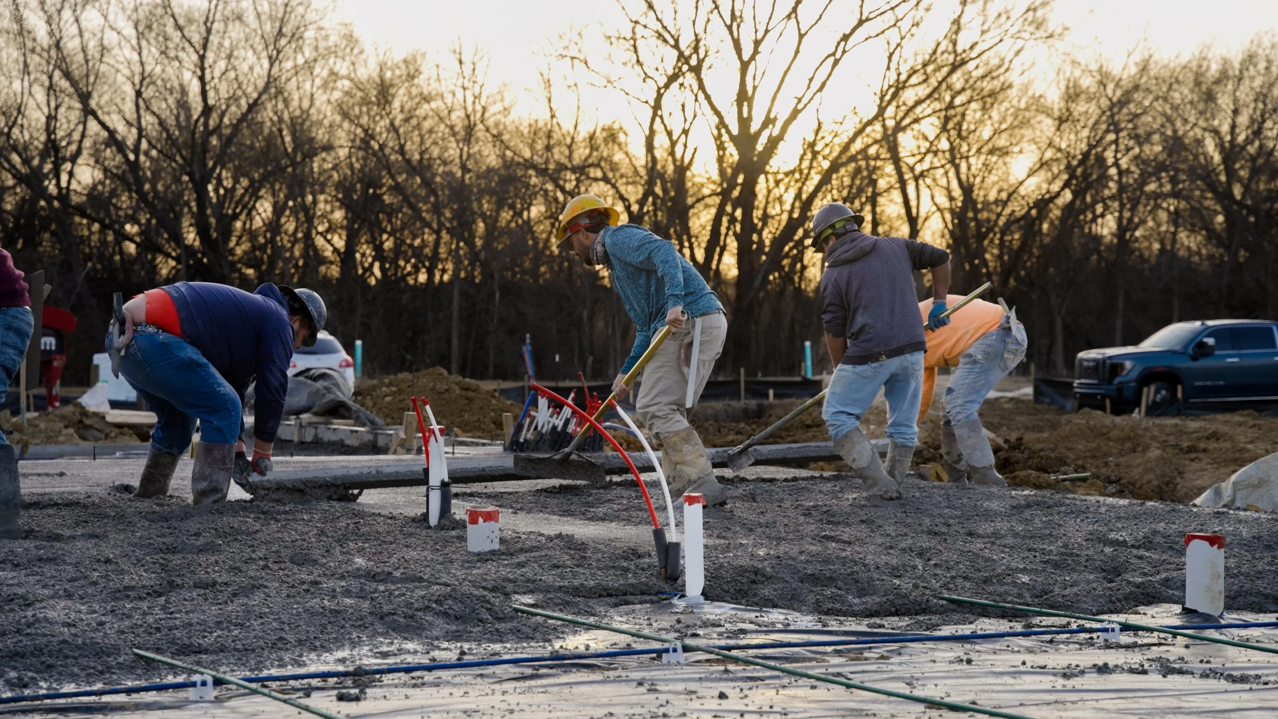 Construction workers pouring and leveling concrete on a building site during sunset.