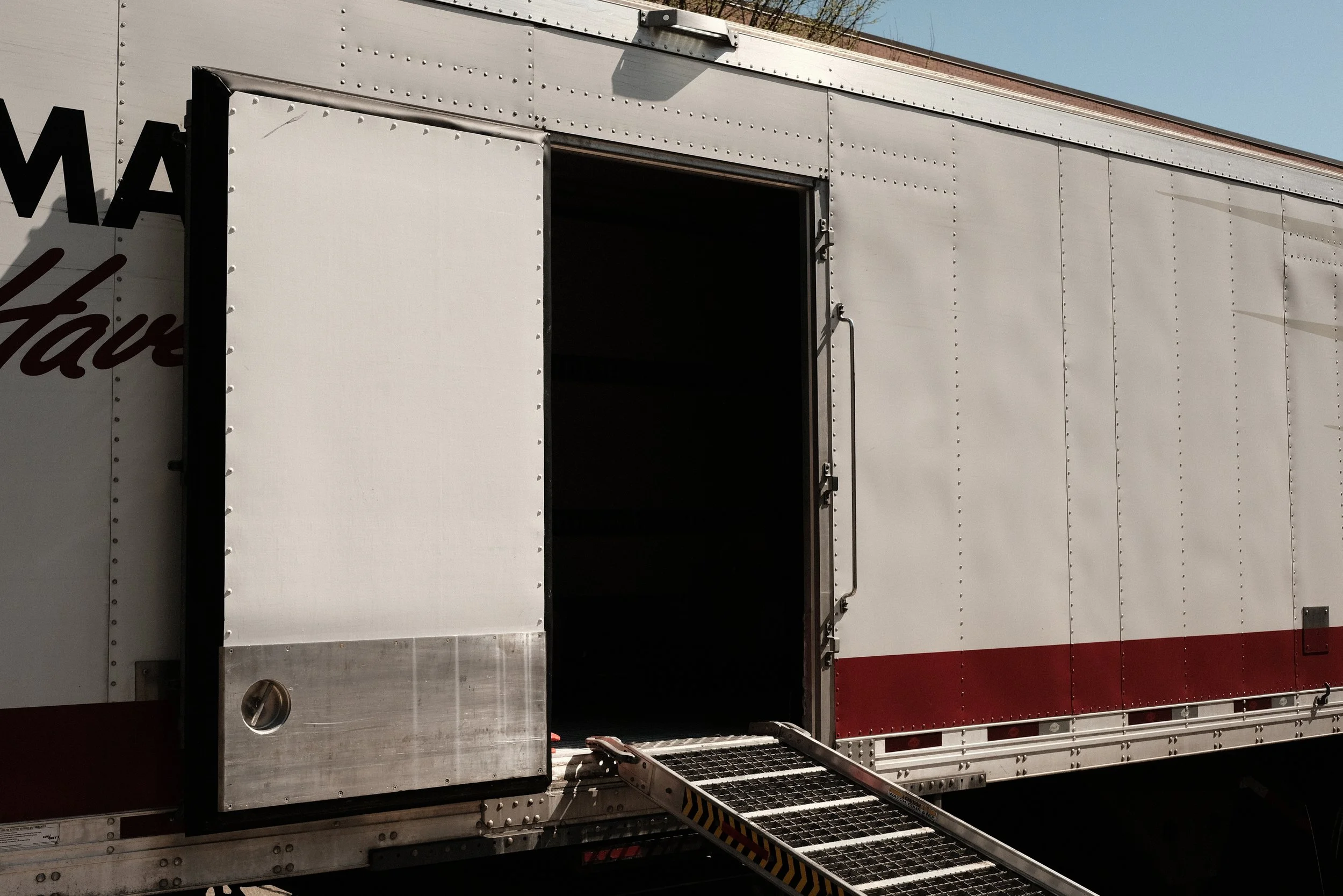 A large, white delivery truck with an open side door and a step ladder extended to the ground.
