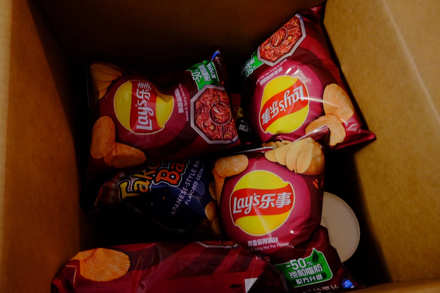 Inside a cardboard box containing three packets of Lay's potato chips and one bag of Farley's potato chips.