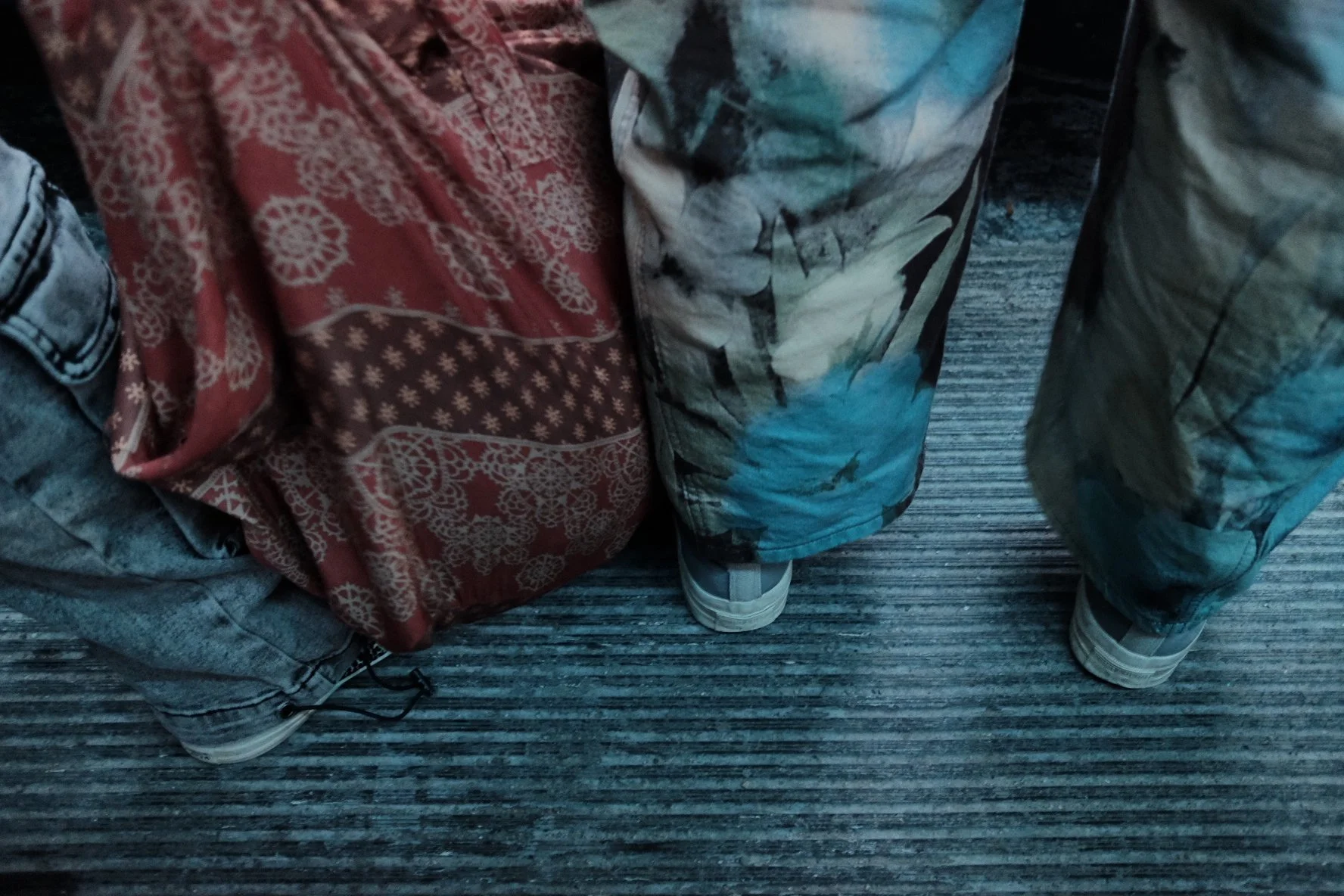 Bottom of two people standing on a carpeted floor, wearing patterned and casual clothing, near backpacks.