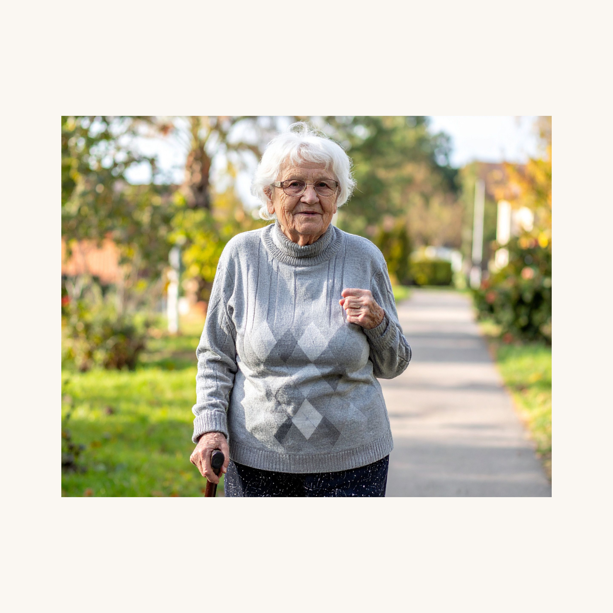 An elderly woman walking outdoors on a sunny day, using a cane and smiling.