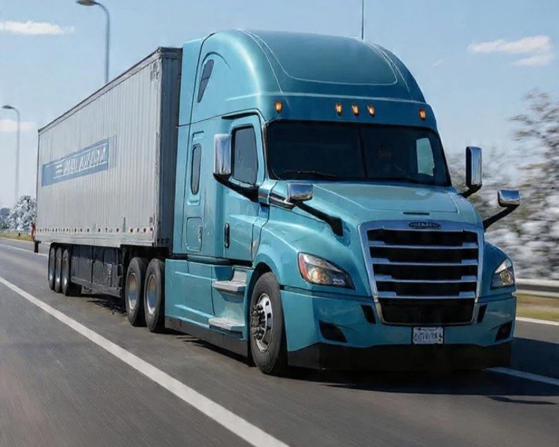 Blue semi-truck driving on highway with trees and blue sky in background.