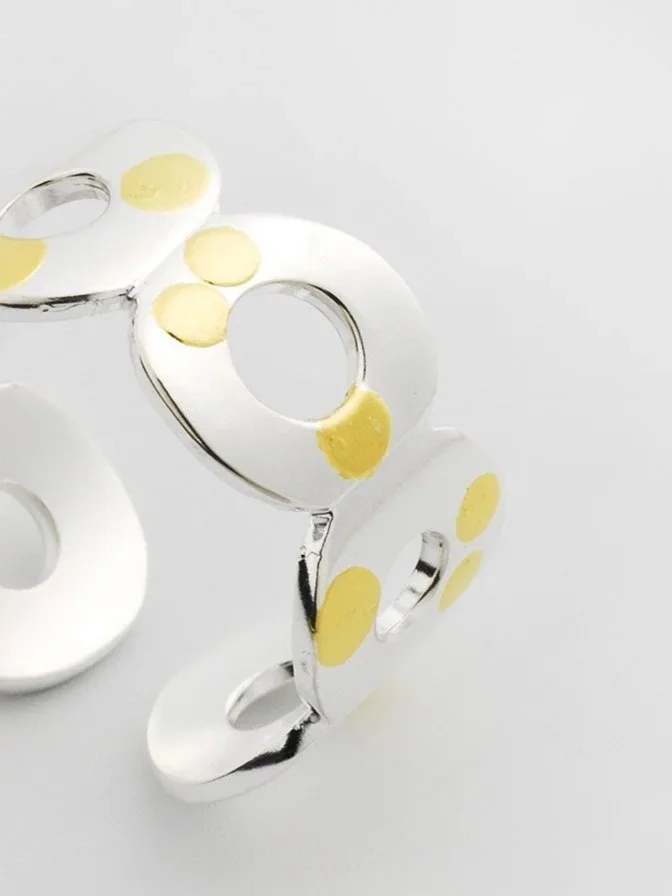 Close-up of Kairoi ring showing connected flat torus forms and scattered gold dot detailing