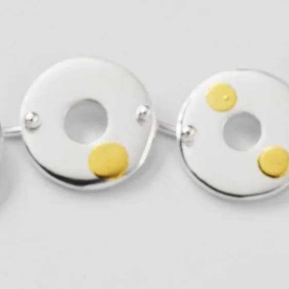 lose-up of Kairoi trio earrings, linked flat torus circular shapes with scattered 24ct gold dotted detail