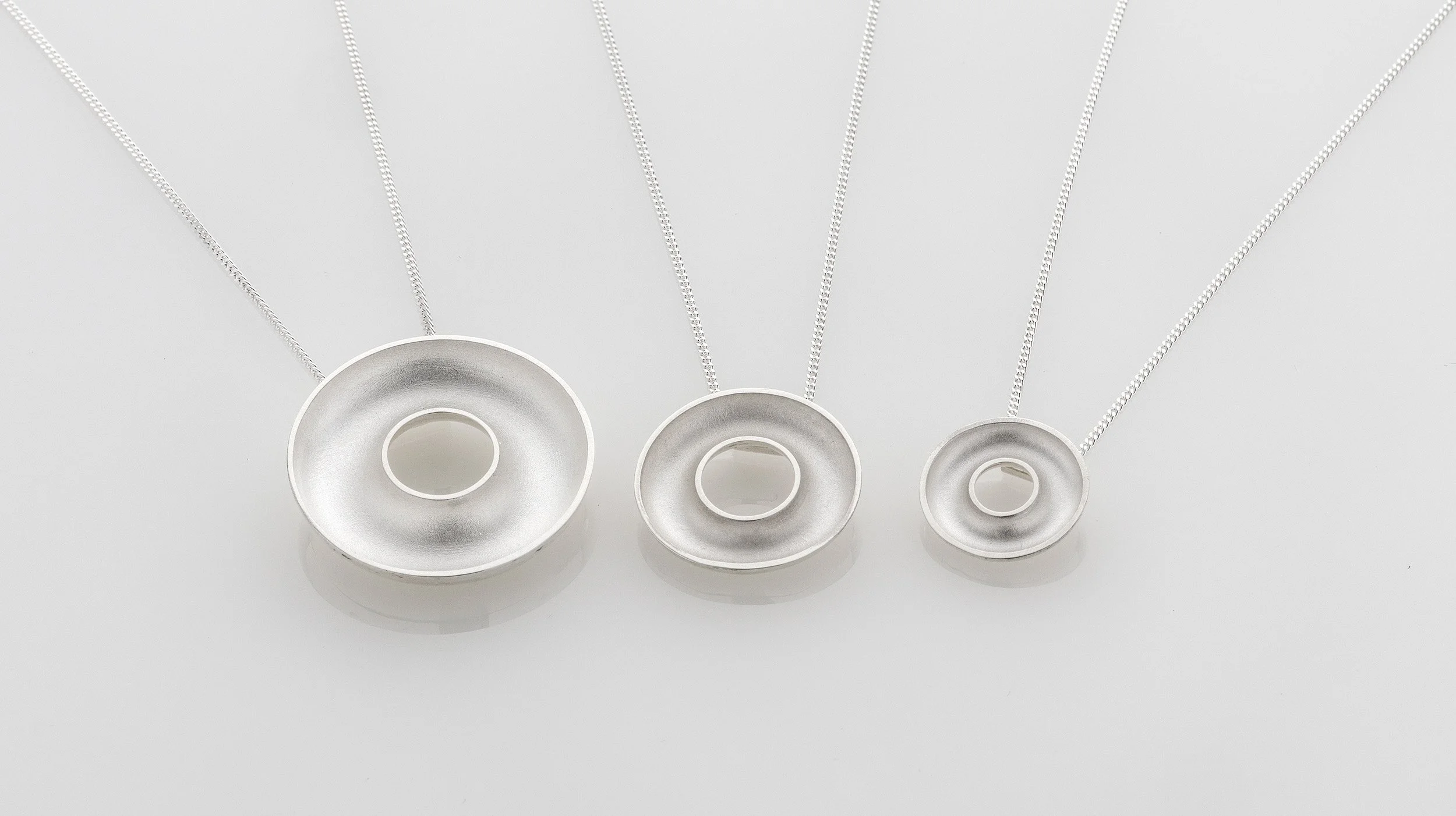 Three sterling silver Orbis necklaces showing large, medium and small concave torus pendants side by side