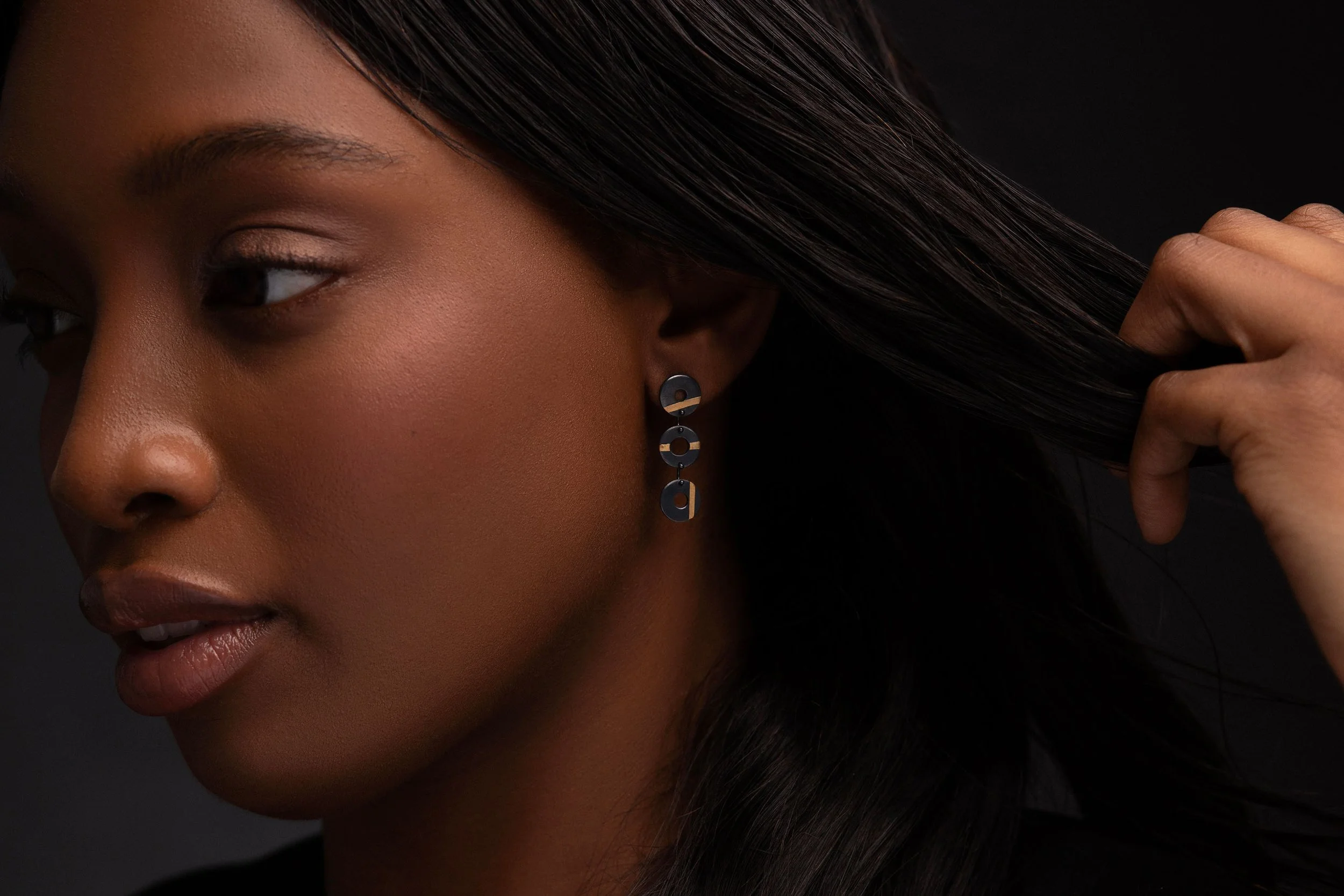 Close-up of model wearing Chronos trio earrings, oxidised silver torus forms with gold stripes