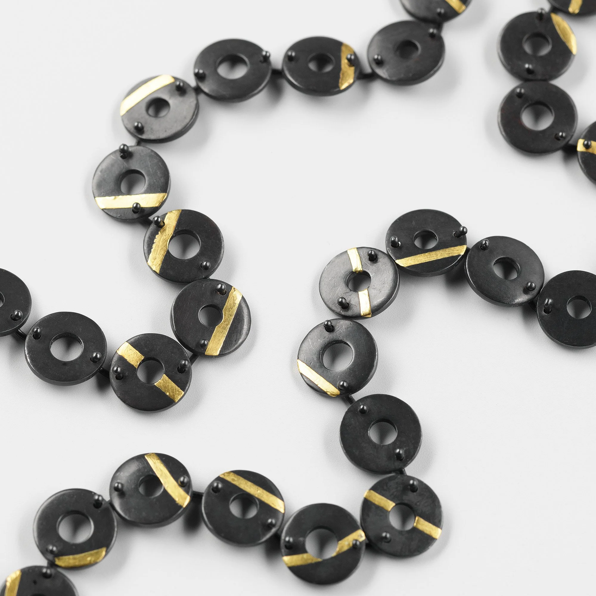 Close-up of Chronos necklace showing oxidised torus forms and gold stripe detail