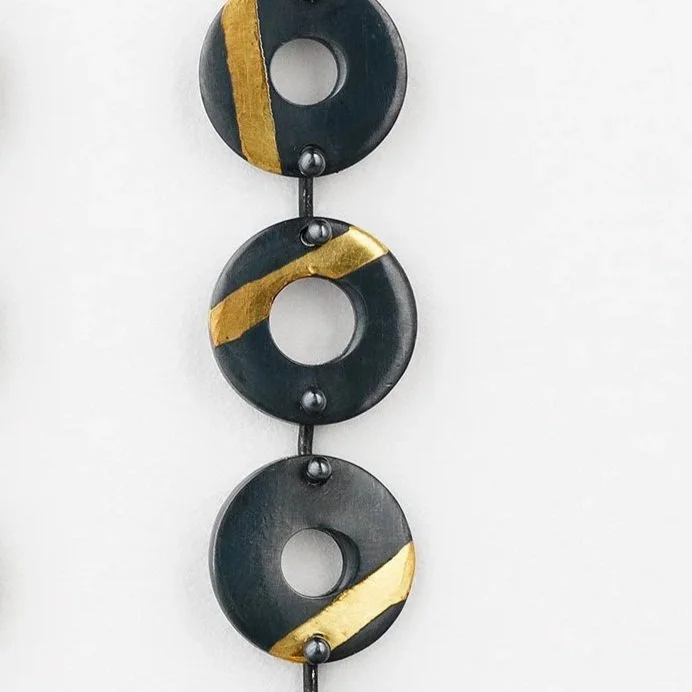 Close-up of Chronos earrings showing oxidised torus forms and gold stripe detail