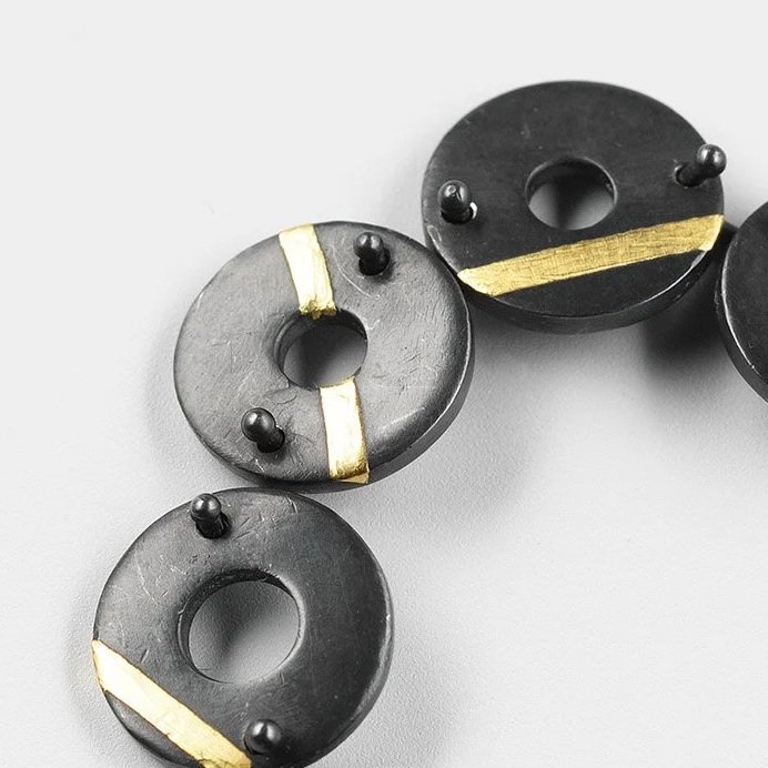 Close-up of Chronos earrings showing oxidised torus forms and gold stripe detail