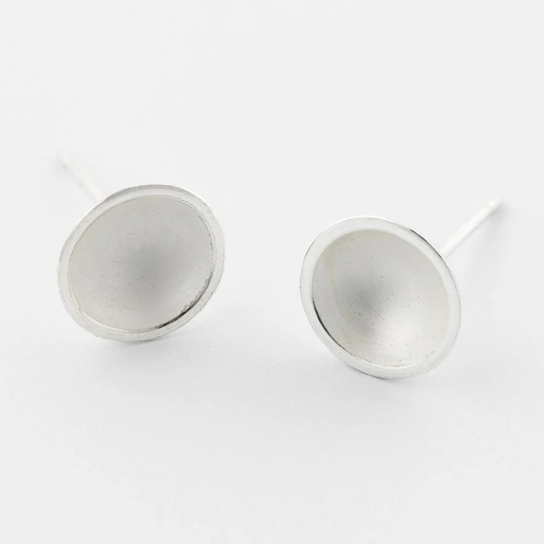 Close up of Small domed sterling silver stud earrings with a soft white interior and polished edge catching the light