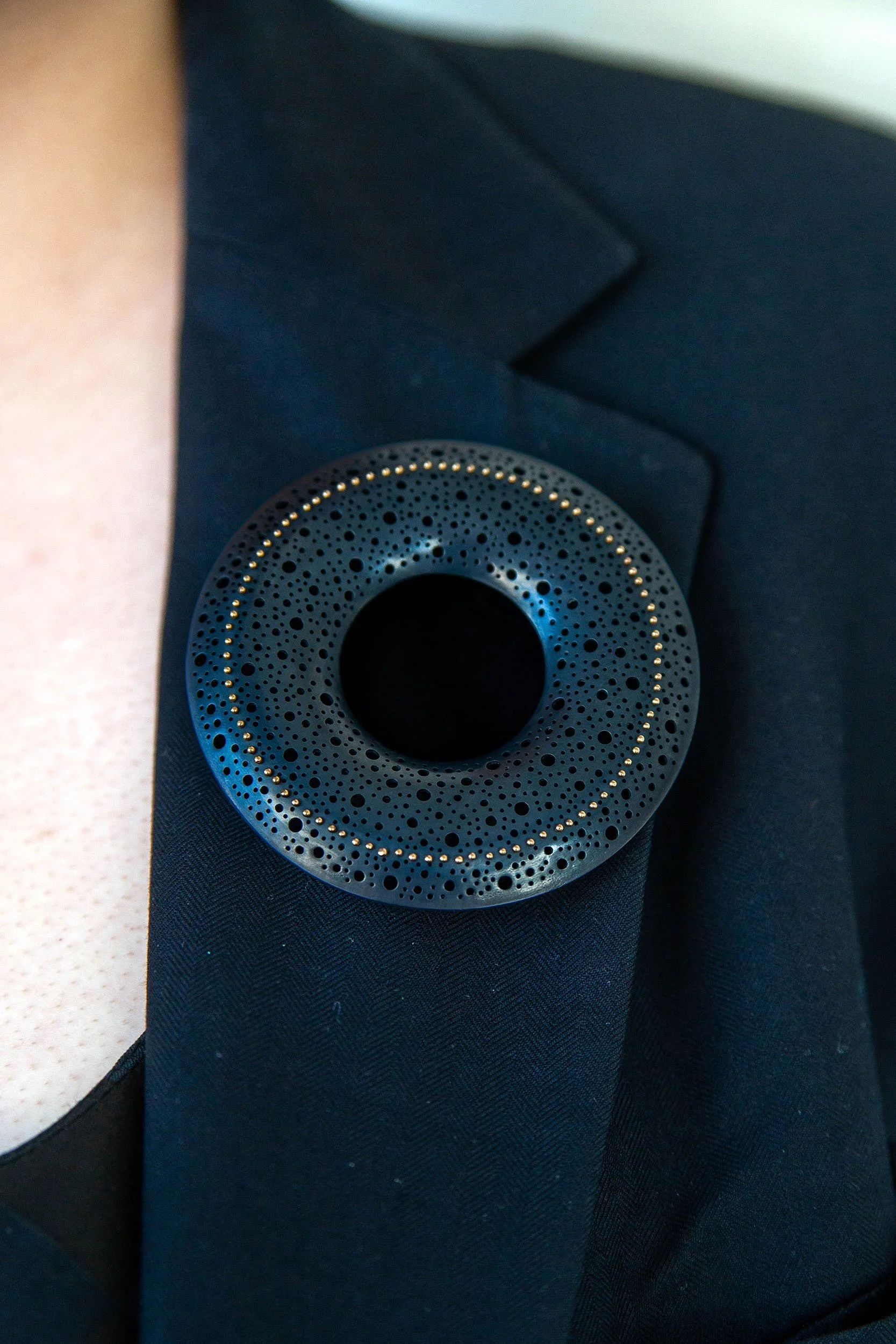 Sum in Black Brooch in oxidised sterling silver with hand-pierced surface and 22ct gold rivet detail worn on model wearing blazer