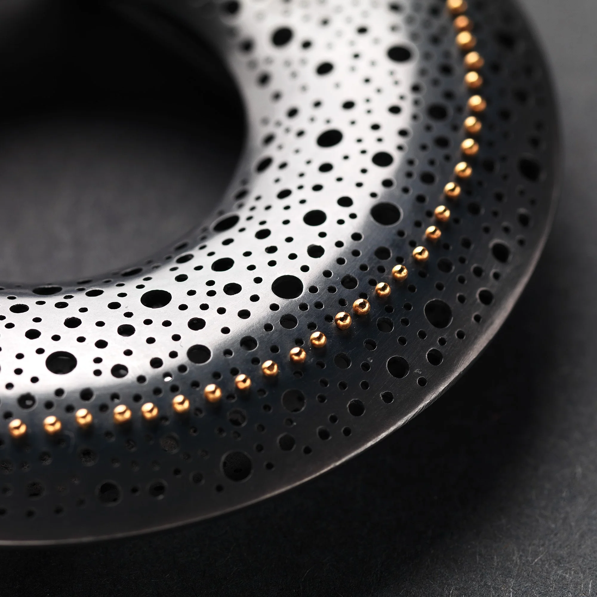 Close up of Sum in Black Brooch in oxidised sterling silver with hand-pierced surface and 22ct gold rivet detail