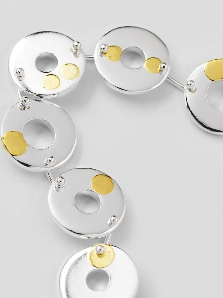 Close-up of Kairoi bracelet showing linked flat torus shapes and scattered gold dot detailing