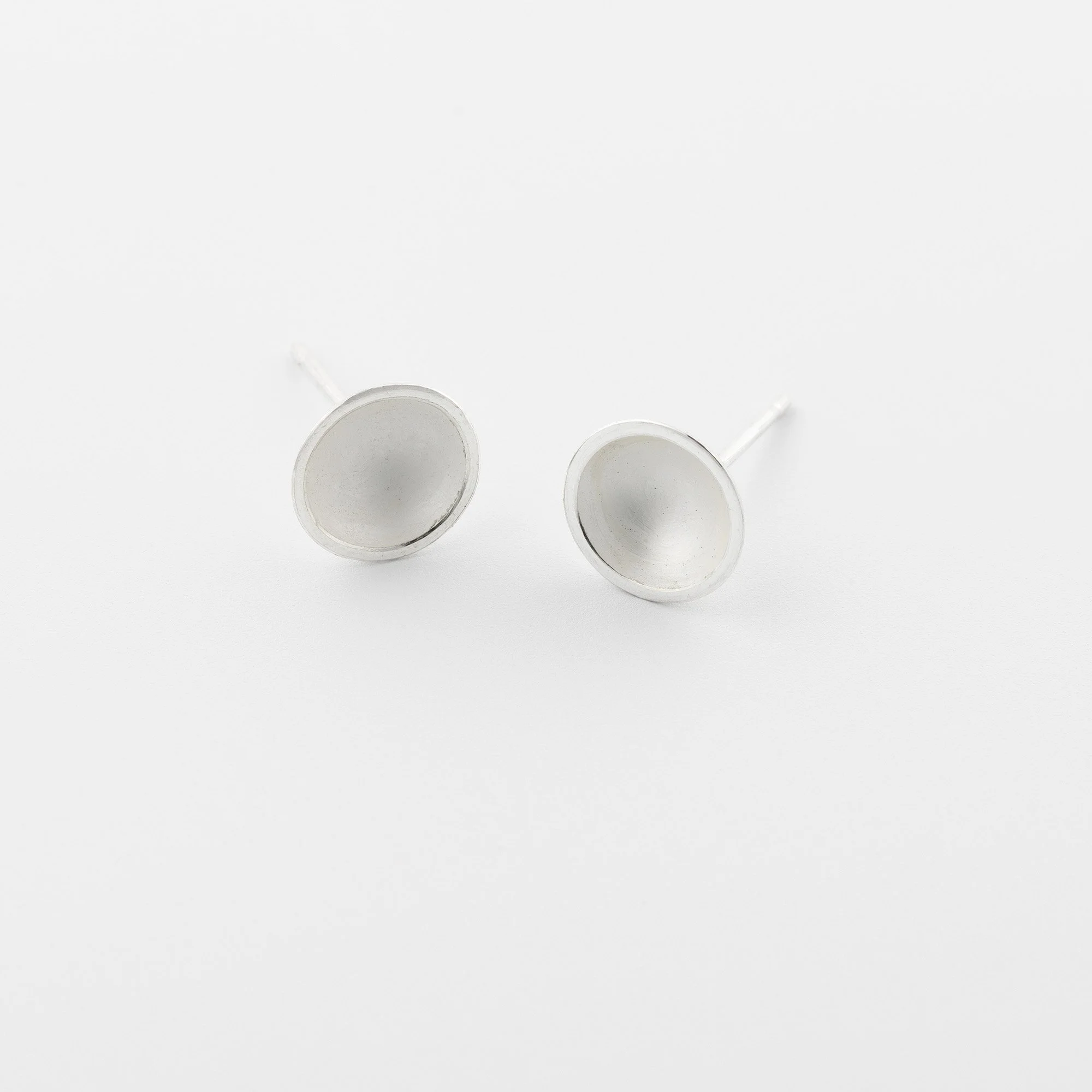 Small domed sterling silver stud earrings with a soft white interior and polished edge catching the light