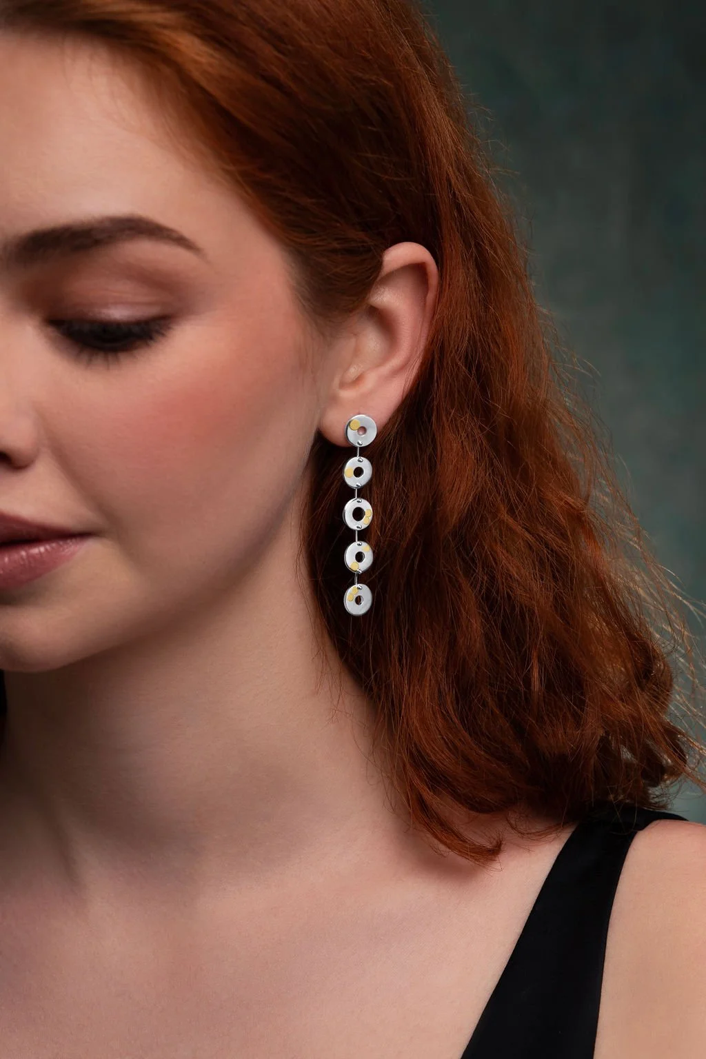 Close-up of model wearing Kairoi earrings, linked flat torus circular shapes with gold dotted detailing