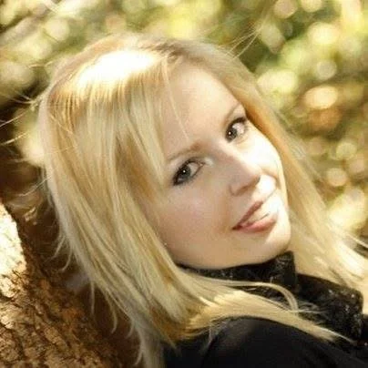 A young woman with blonde hair smiling outdoors.