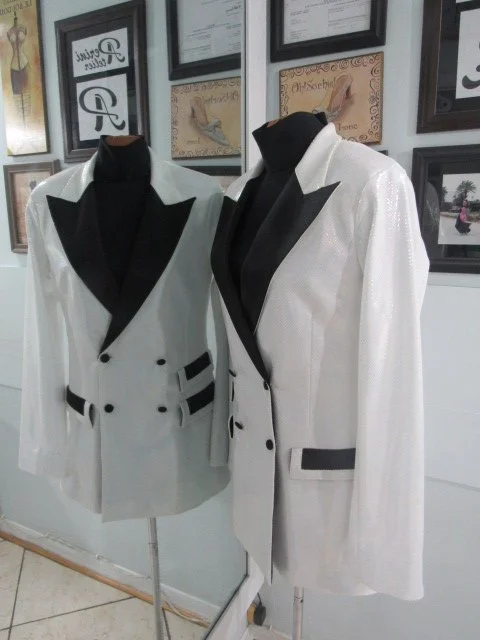 Two white tuxedo jackets with black lapels and details displayed on mannequins.