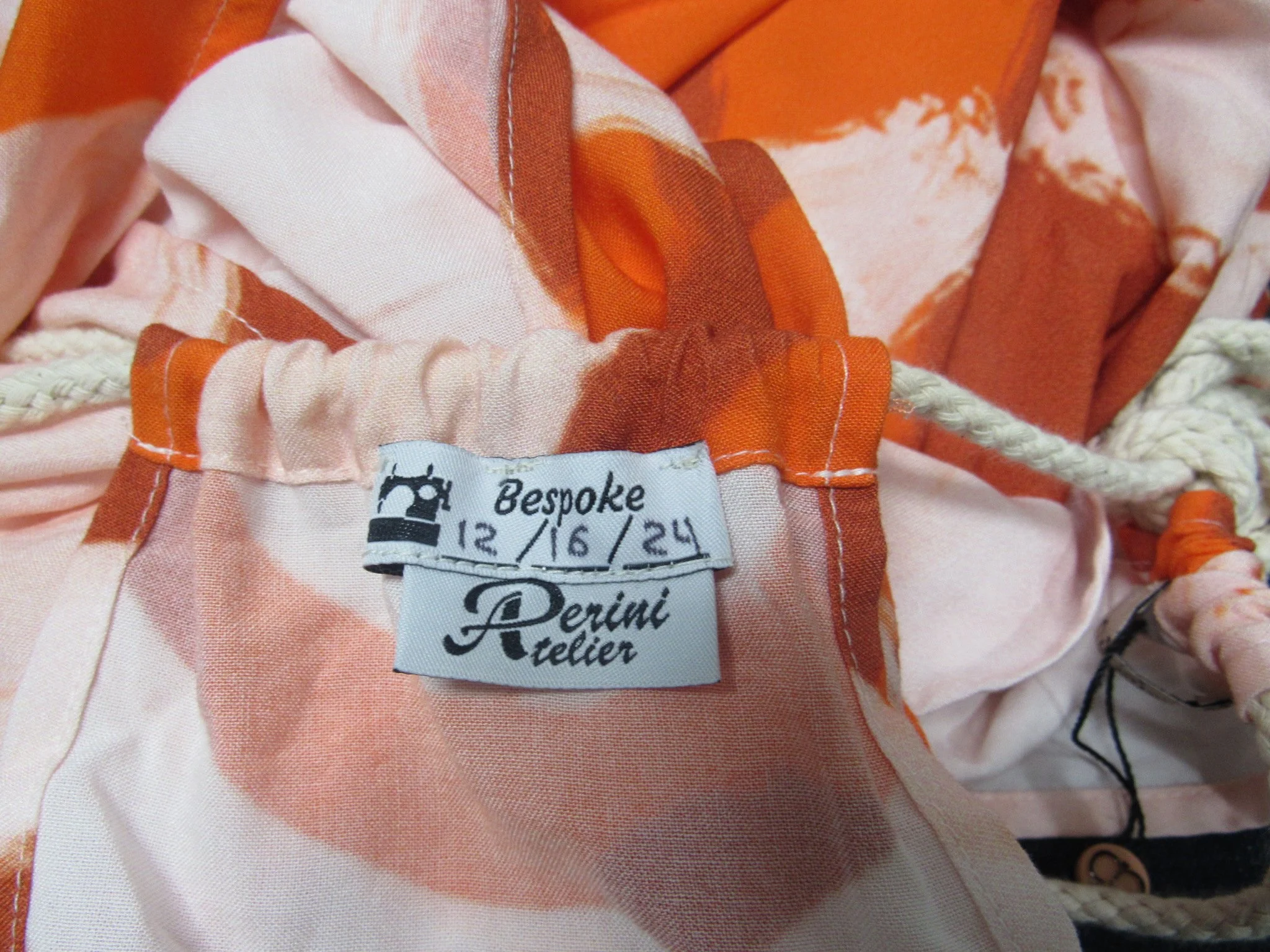 Clothing label inside an orange and white patterned garment, indicating it is a bespoke piece made by Perini Atelier, with size measurements 12/16/24.