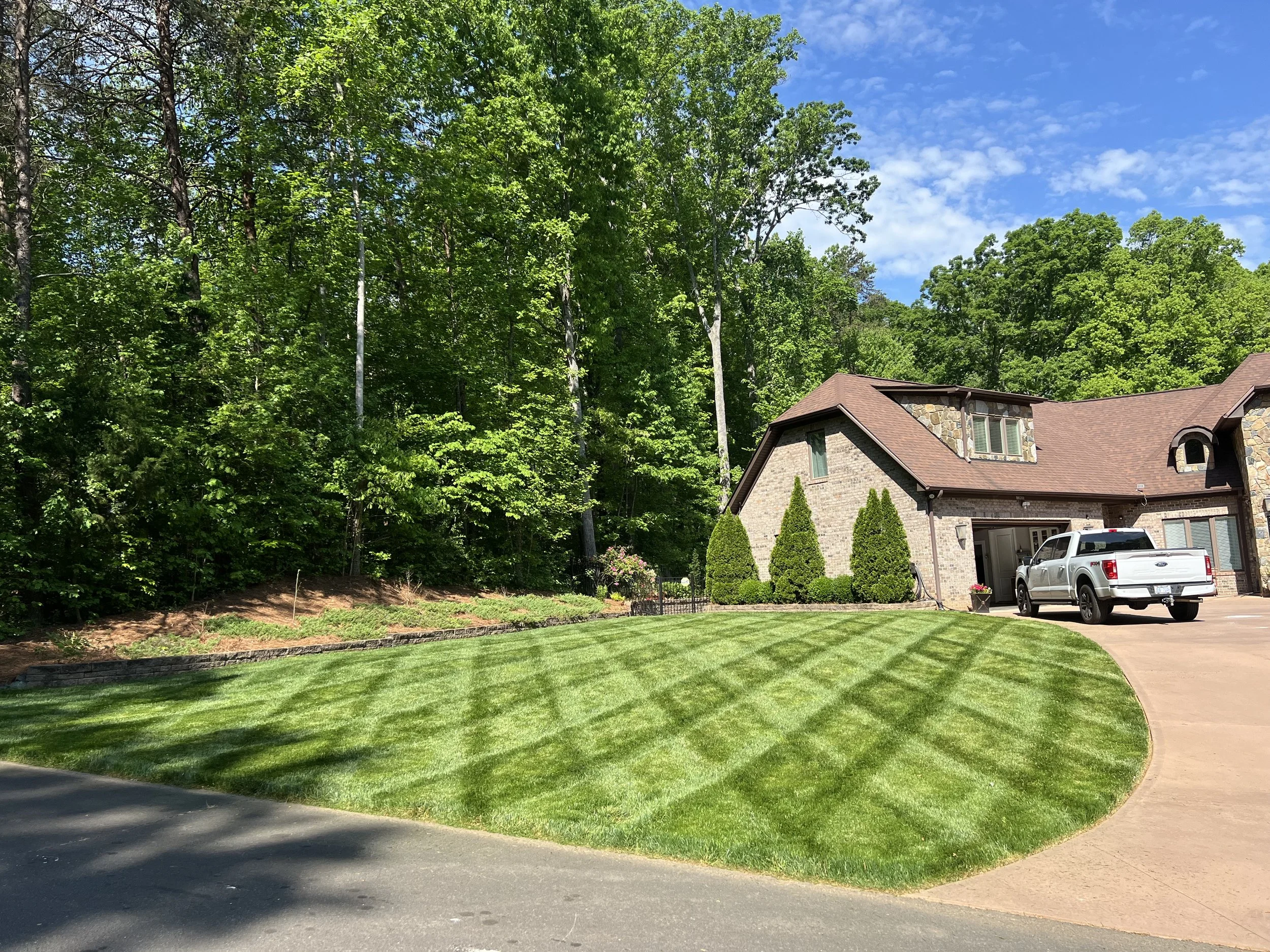 A house with a well-maintained lawn and a driveway, surrounded by trees and greenery on a sunny day.