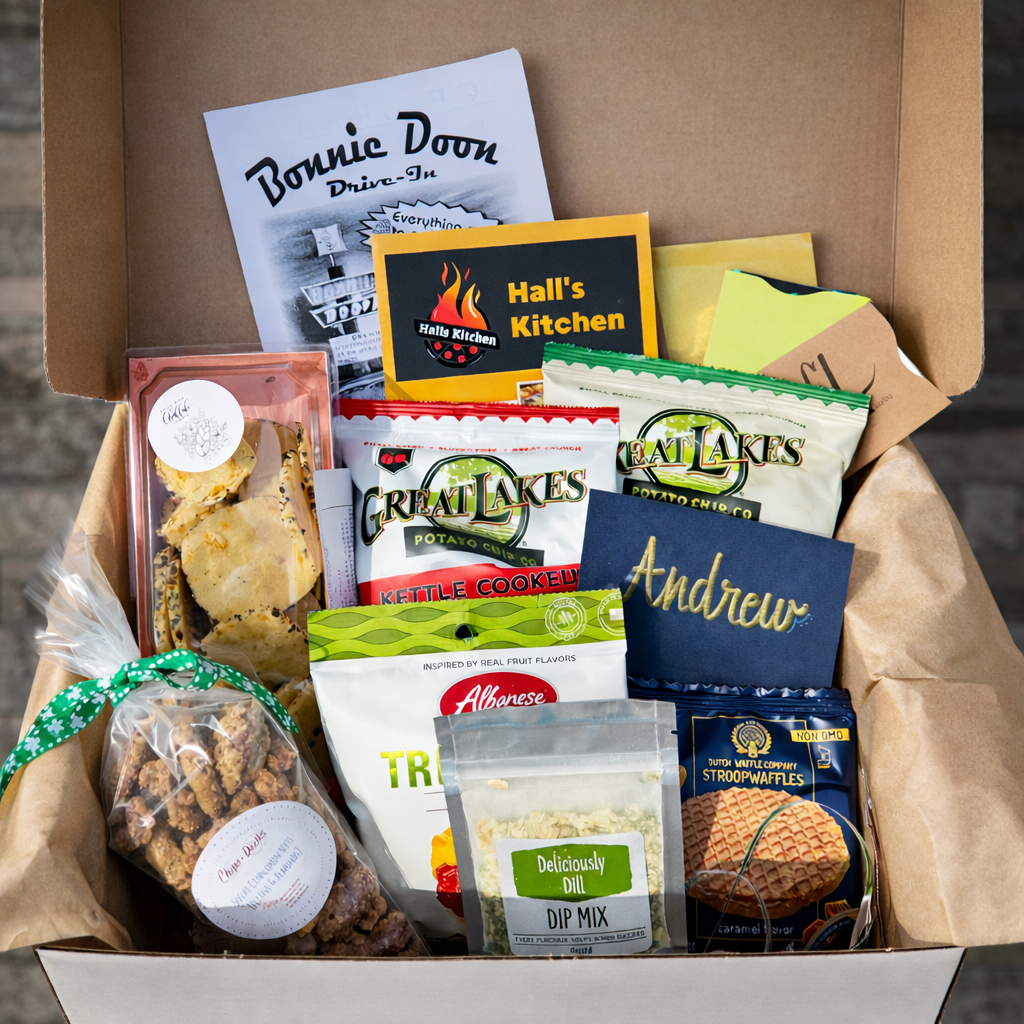 A gift box filled with snacks and treats including chips, cookies, waffle mix, and a bag of trail mix, with a blue gift card and other paper items inside.