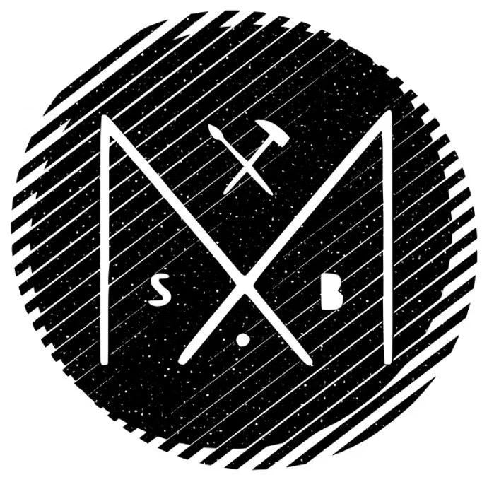 A black circular logo with white lines, stars, and moon patterns. It features two crossed tools (a wrench and a hammer), with the letters S and B on opposite sides. There is a small white dot at the bottom center.