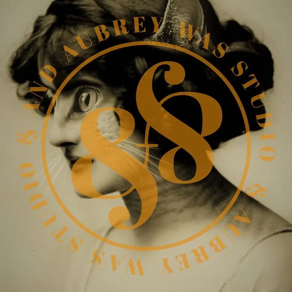 A woman with short curly hair and a headband, looking to the side, with a circular overlay containing the text 'AUBREY WASS STUDIO' and the number 48.