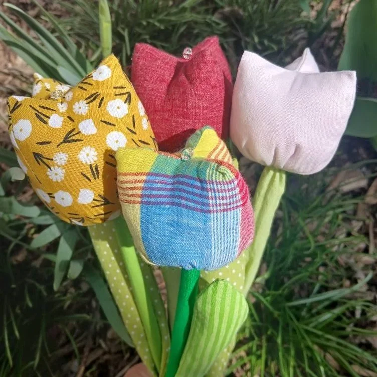 Four tulips made of fabric with different patterns and colors, arranged on green stems with leaves, set against grass and soil.