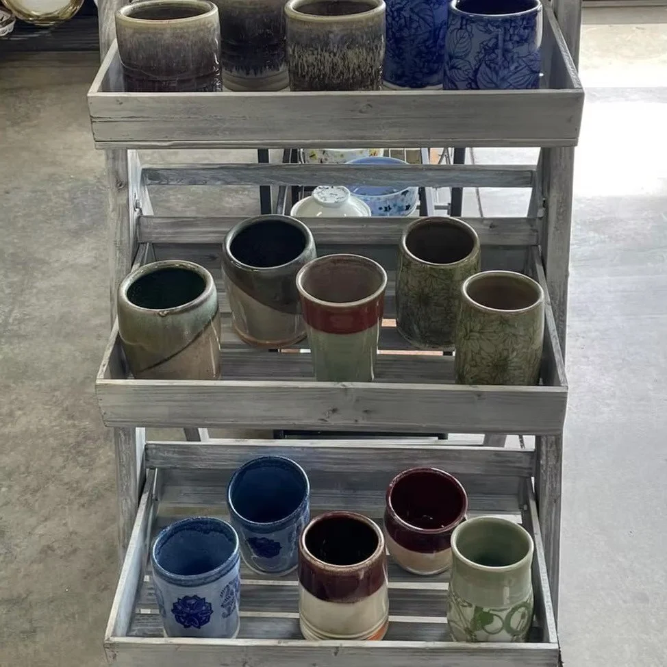 Display of various ceramic cups on a white wooden shelf in a store.
