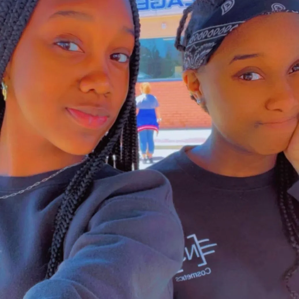 Two young women with braided hair taking a selfie outdoors, smiling.