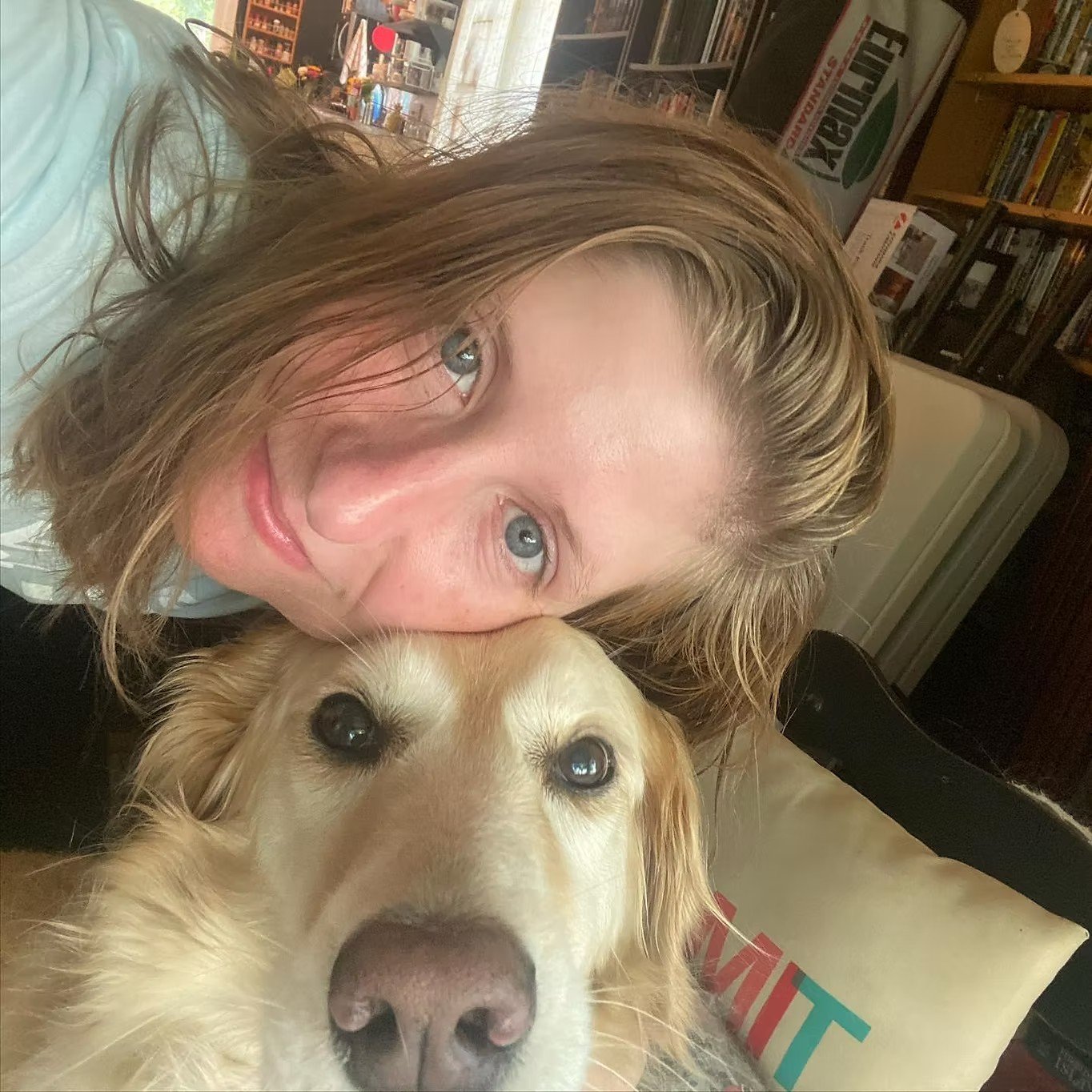 A woman with brown hair and blue eyes hugging a yellow retriever dog with similar blue eyes.