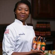 A woman dressed as a chef holding bottles of hot sauce.