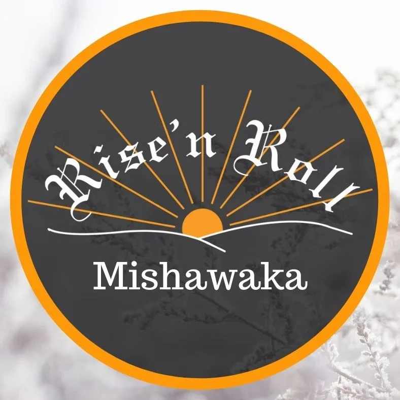 A circular logo with an orange border and black background featuring a stylized sunrise with radiating lines, the words 'Hízám' and 'Roy' in stylized font, and the name 'Mishawaka' written below.