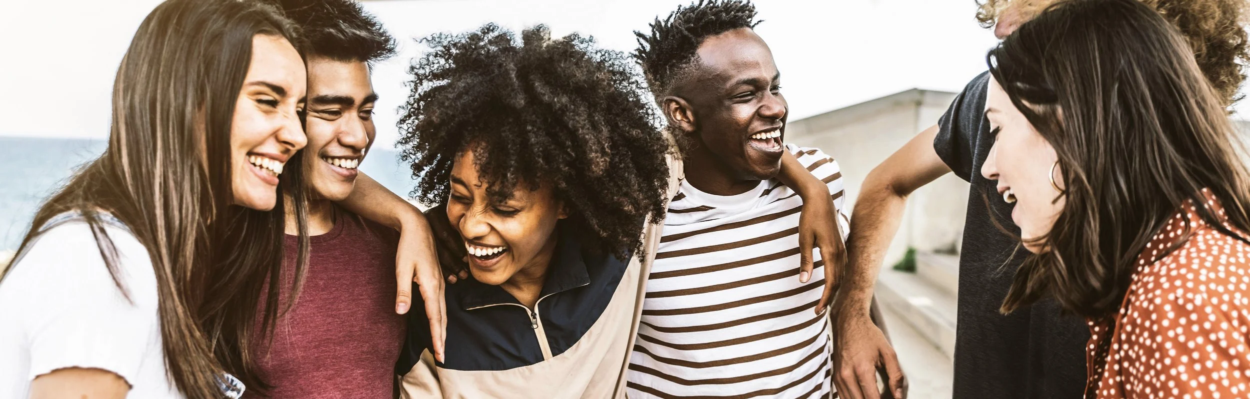 Group of six diverse friends smiling and laughing together outdoors.