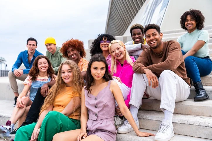 Group of diverse young adults sitting on outdoor stairs smiling at the camera
