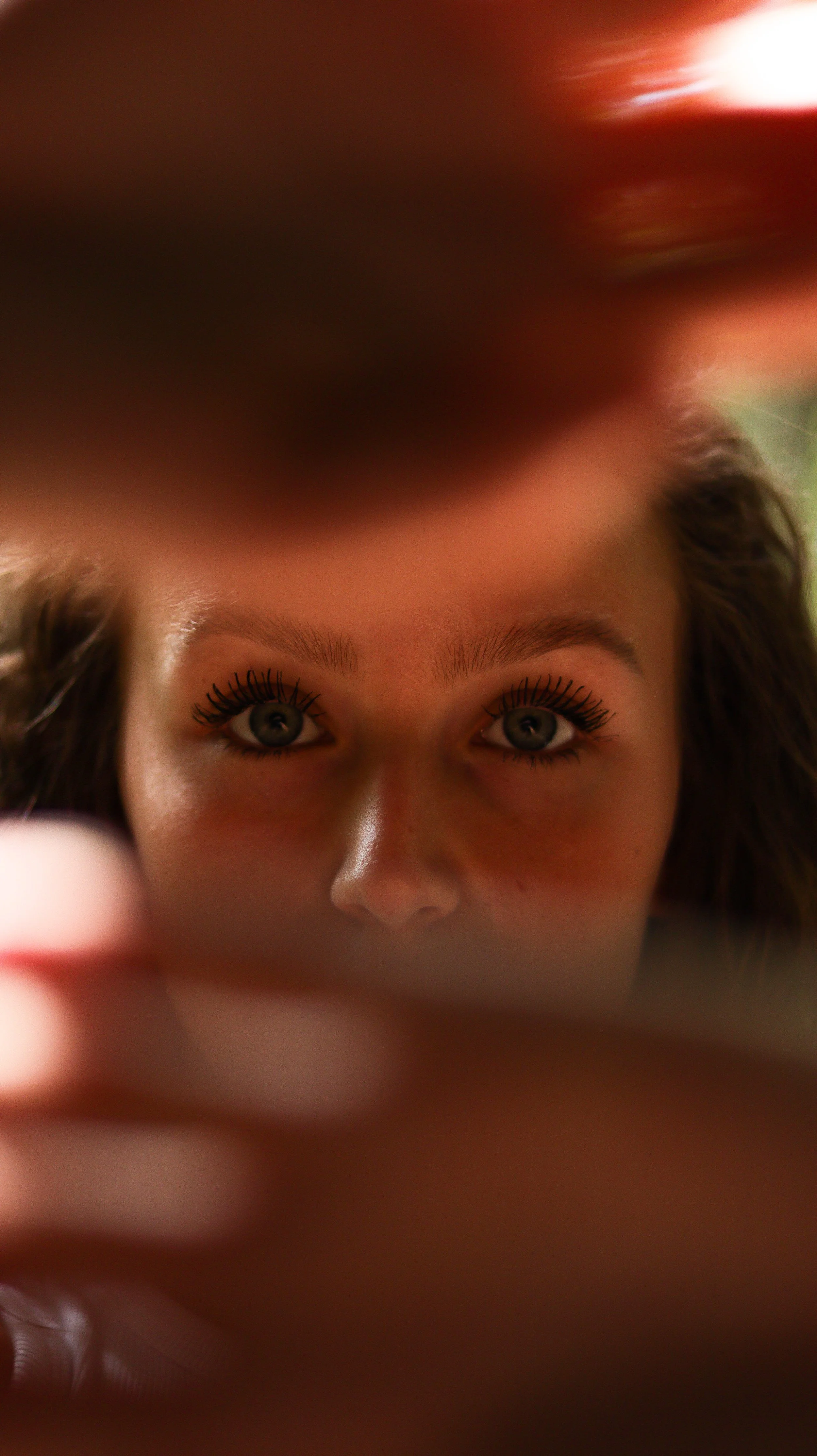 Close-up of a woman's face, with bright eyes framed by long eyelashes, seen through an opening made by fingers.
