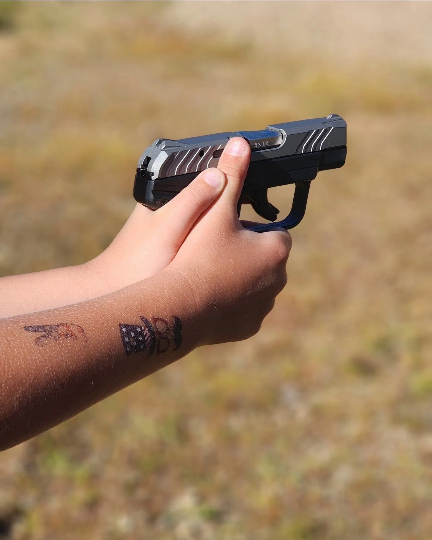 A person holding a handgun with a desert background.