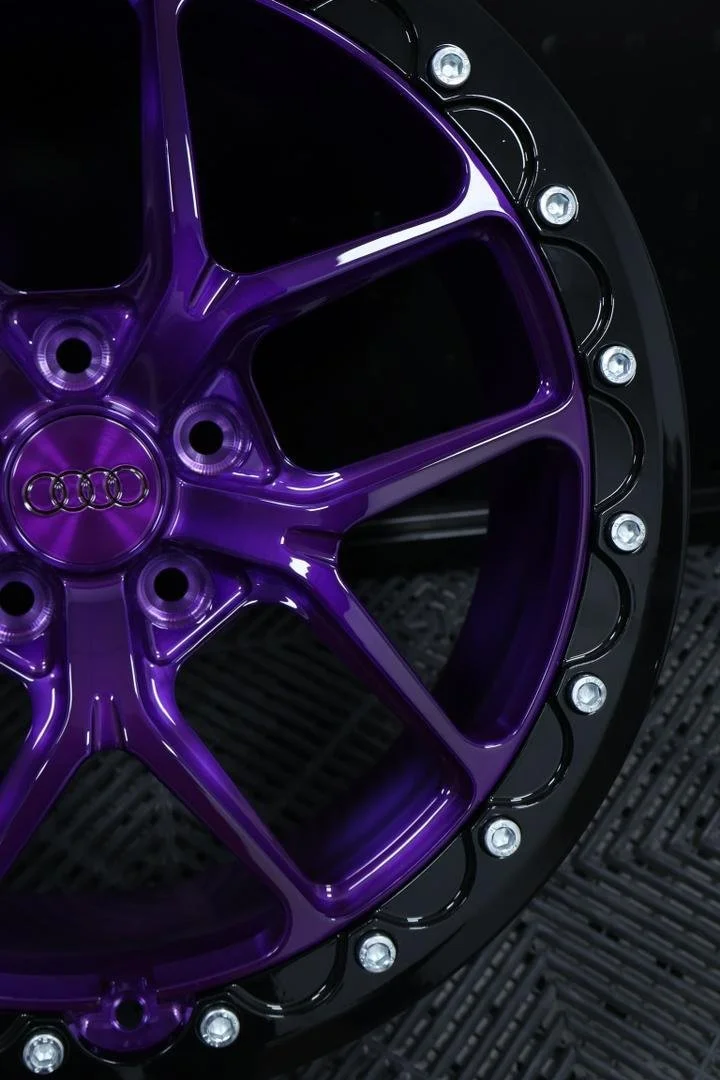 Close-up of a purple and black car wheel with the Audi logo in the center, featuring a sleek design and embedded lights around the rim.