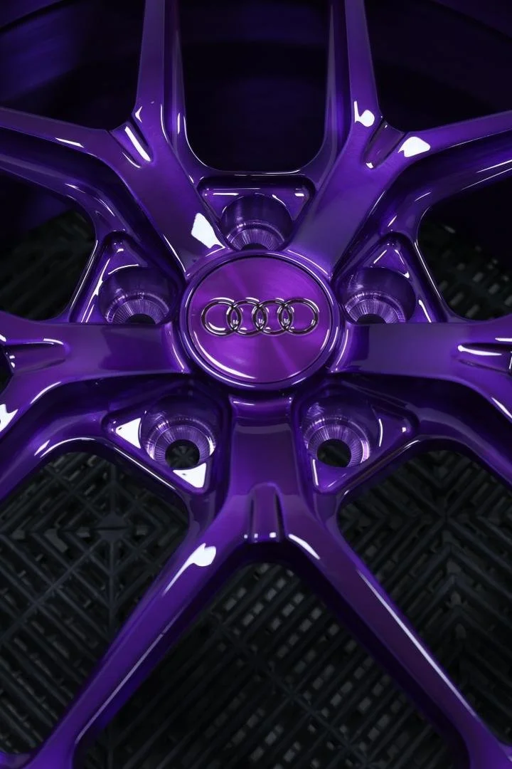 Close-up of an Audi car wheel rim painted in glossy purple with the Audi logo in the center.