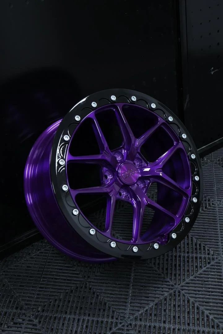 A purple and black car wheel rim with bolt accents leaning against a black wall on a black textured floor.