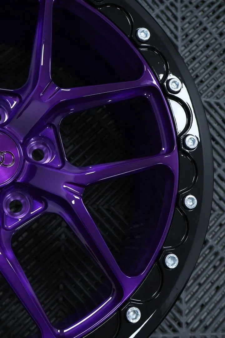 Close-up of a purple alloy wheel with silver bolts, on a black vehicle rim.