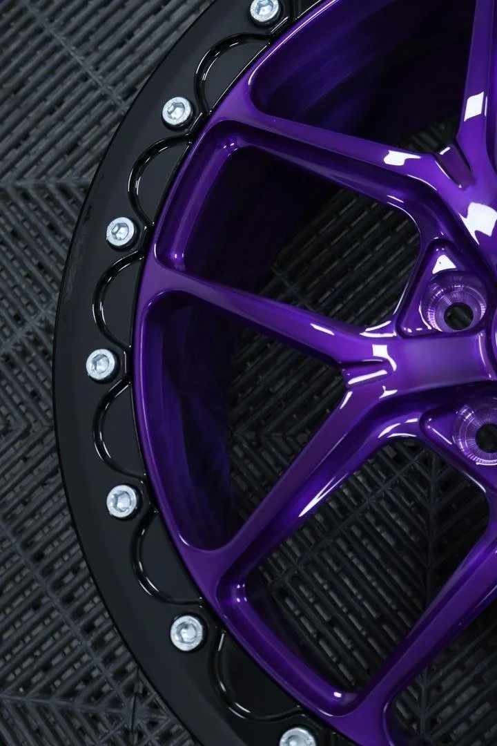 Close-up of a purple and black wheel rim with silver bolts on a black textured surface.