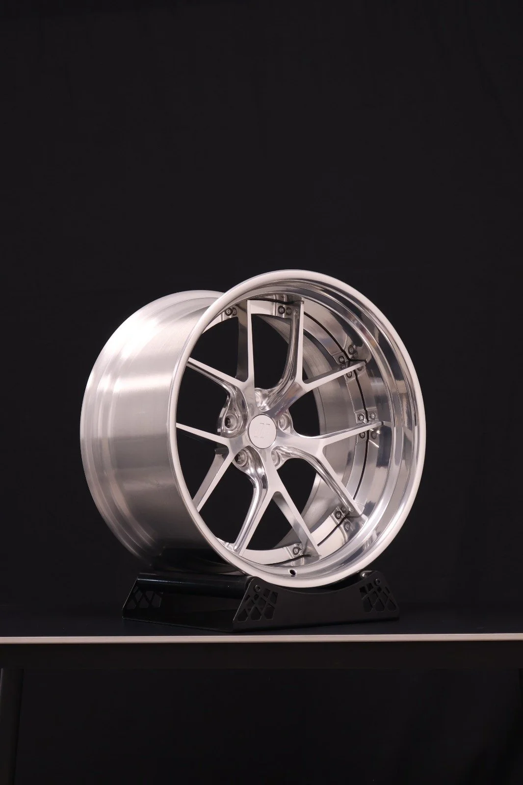 A shiny, silver, multi-spoke alloy car wheel rim on a black display stand against a black background.
