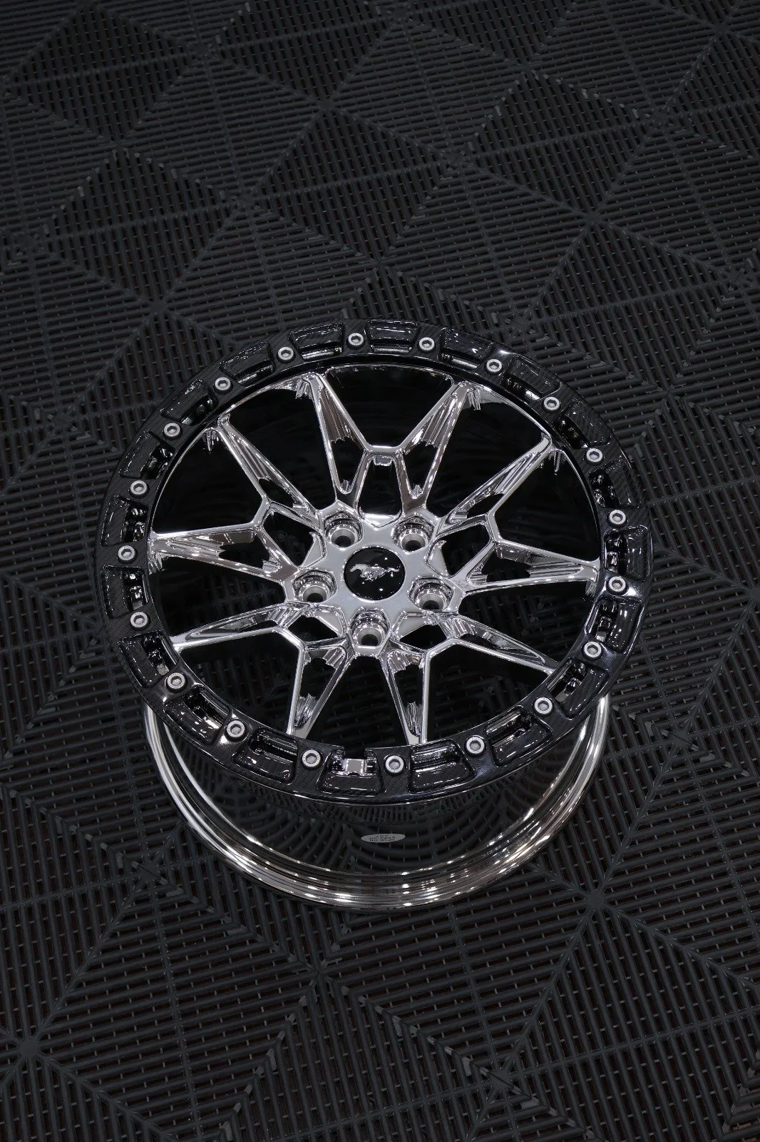A chrome and black car wheel rim placed on a black rubber mat with a textured pattern.